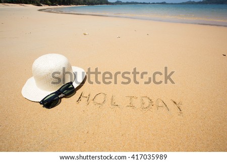 Holiday written in the sand at the beach waves in the background.
