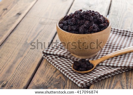 Dried raisins in wooden cup and spoon on wooden table. Royalty-Free Stock Photo #417096874