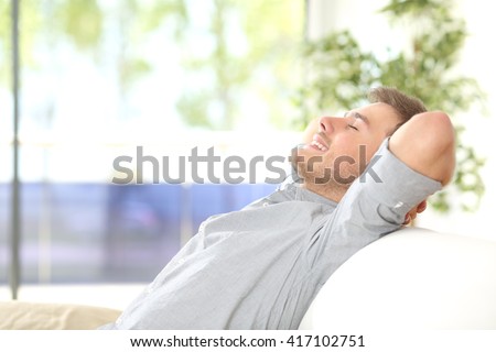 Side view of a happy attractive man resting and breathing sitting on a couch at home with a window with a green background outdoors Royalty-Free Stock Photo #417102751
