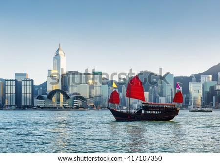 Beautiful view of traditional Chinese wooden sailing ship with red sails in Victoria harbor at evening. Skyscrapers in downtown of Hong Kong are visible from Kowloon side. The Hong Kong Island skyline