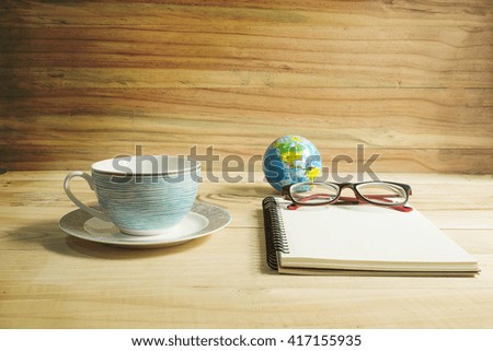 Place the empty coffee cup and note book on  wooden table.