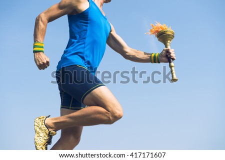 Torchbearer athlete in blue running with ceremonial sport torch across sunny blue sky Royalty-Free Stock Photo #417171607