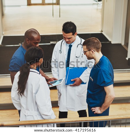 Multiracial group of doctors in an impromptu meeting standing on a stairwell looking at information on a tablet computer, view from above