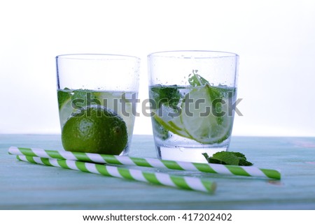 Two glasses with cocktail and ice with lime slice on table.