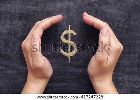 Hands protecting drawn dollar sign on black chalkboard background. Close up.