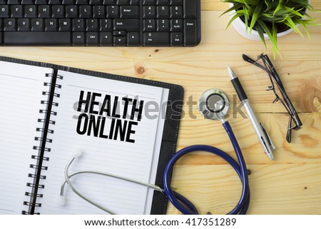 Medical Concept - Stethoscope with notebook written Health Online with keyboard, green plant, a pen and spectacle on wooden background
