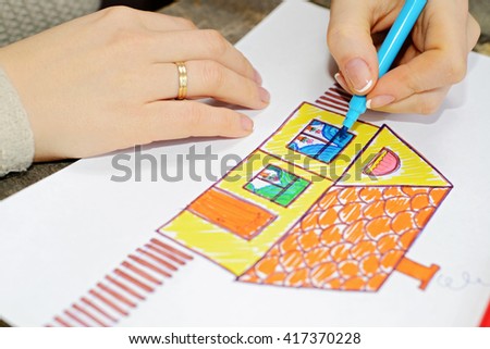 Close up of the hands of woman drawing a house with color pencil