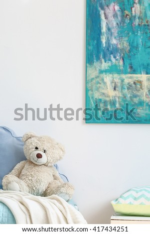 Fragment of a light room with abstract painting on the wall and a beige teddy bear on a blue bed