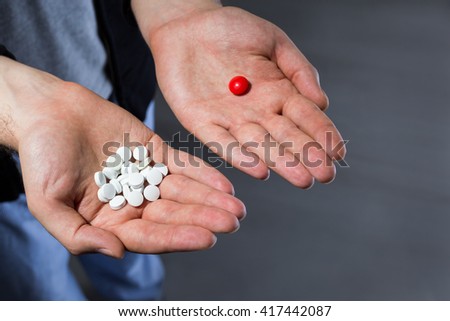 Man with pile of white pills in one hand and a red pill in another