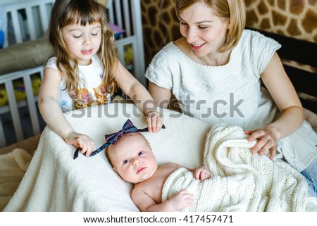 Young mom with her 5 years old daughter and 2 months old baby  and playing in the bed at the weekend together