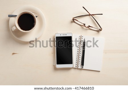 Opened notebook with blank area, pen, smart phone, and coffee cup on wood table in morning time