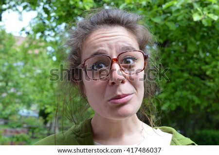 Nerd woman with big dioptets dusty glasses, lush green trees background