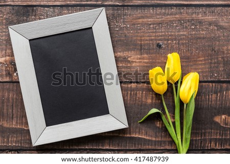 Light frame and bouquet of yellow tulips lying on rustical, wooden board