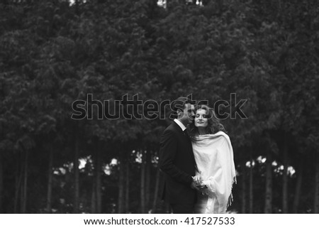 Man holds woman in shawl in the front of the forest