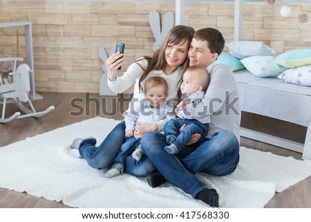 family and technology concept - happy parents and little boys twin taking selfie by smartphone in room