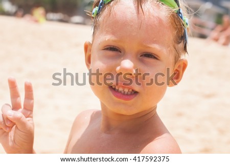 Wet Adorable Child Boy with Goggles After Bathing Sea Shows Sign Two Fingers Hand Peace
