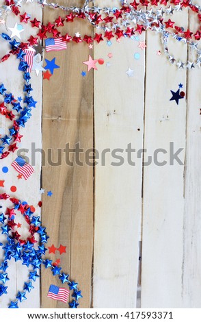 Red, silver and blue stars, spangles and US flags create a border around a rustic wooden background. The wooden planks and varied in tone and run vertically. Copy space available