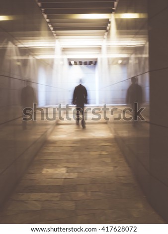 Blurred image of a man walking in an underground passage. Man walking away in a under passage to the light. Toned image. Motion blur.