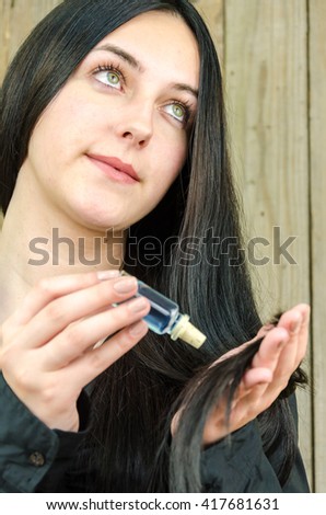 Beautiful teenager lubricates and nourishes the hair with an ampoule and drops the hair on the old wooden background