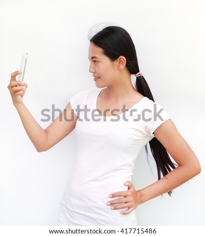young girl taking pictures of herself through cell phone on white background