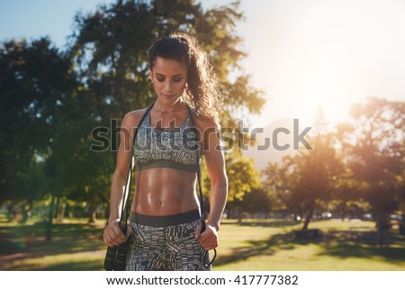 Fit and athletic young woman standing in a park with a jump rope. Young woman aerobics instructor with jumprope. Royalty-Free Stock Photo #417777382