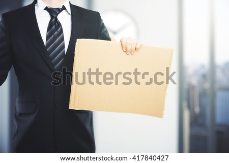 Businessman with blank carton board in blurry office interior. Mock up