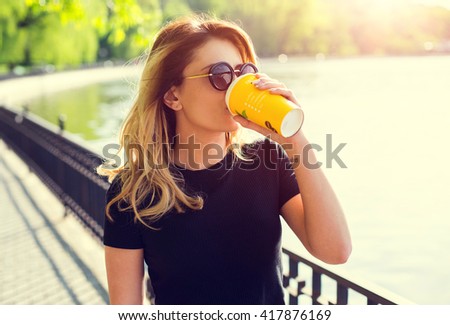 Portrait of a girl in sunglasses with a paper cup of coffee . Shooting at sunset