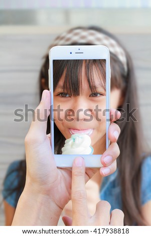 Hand man with Smartphone taking a picture of Asia girl child eat ice cream in restaurant.