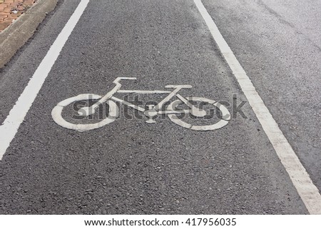 White bicycle sign on asphalt bike lane parallel car road