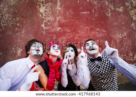 Four mimes point to the top on a red wall.