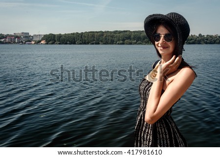 happy stylish woman hipster holding hat and smiling at sunny shore, summer travel concept, space for text