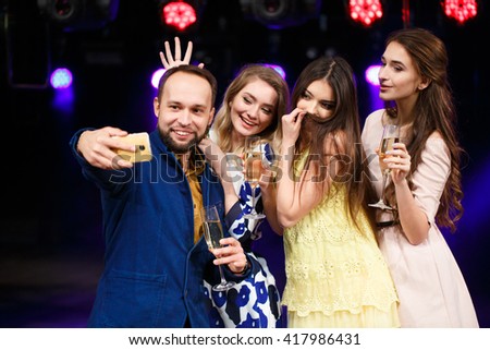 party, holidays, technology, nightlife and people concept - smiling friends with glasses of champagne and smartphone taking selfie in club