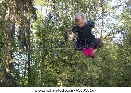 Little child blond girl having fun on a swing outdoor. Summer playground. Girl swinging high 