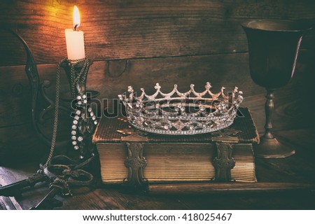 low key image of beautiful diamond queen crown on old book, burning candle. vintage filtered. fantasy medieval period
