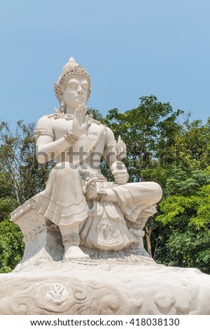 The Statue of Thai angel is white cement sculpture in the Thai temple of Thailand with green nature background.