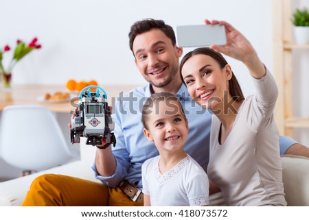 leave it for the memories. Cheerful delighted loving family sitting on the couch and making photos while playing with robot 