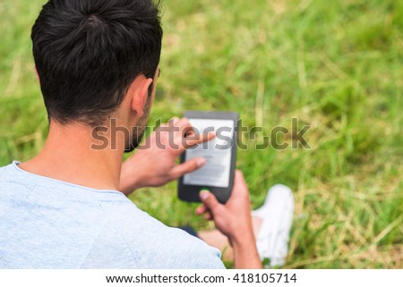 Young man sitting in the green grass and using tablet on a sunny day