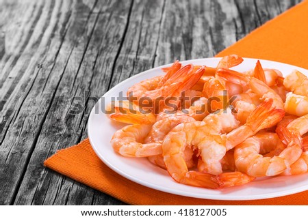boiled tails of king shrimps on a white bowl on a dish with orange table napkin, close-up
