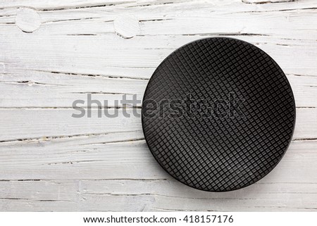 Round black plate on white wooden background. The plate is placed in the right lower corner. The wood is a bit weathered.
