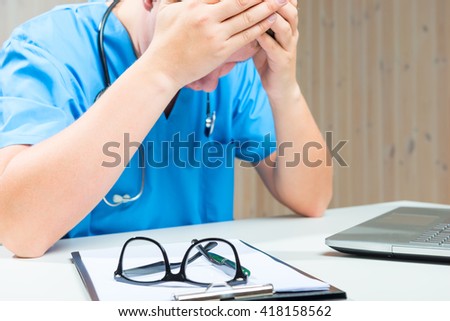 focus on the glasses, tired Doctor sits at a table out of focus