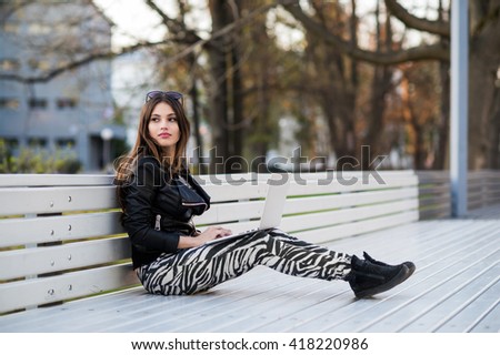 Close portrait of gorgeous dark-hair female student using laptop computer at campus, charming female teenager studying on park bench with open net-book, exam preparation