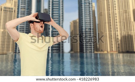 3d technology, virtual reality, entertainment and people concept - happy young man with virtual reality headset or 3d glasses playing game over dubai city infinity edge pool background