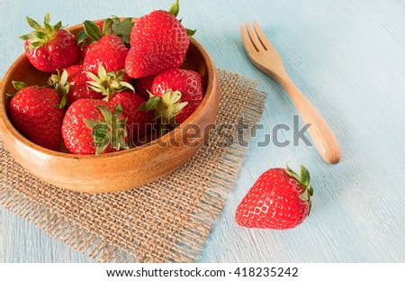 Ripe red strawberries in bowl on wooden table, close up