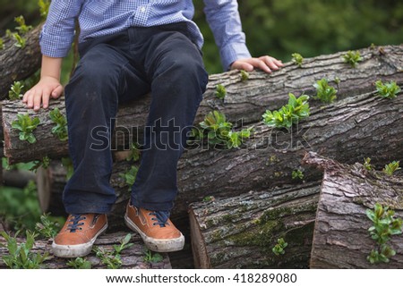 Adorable kid boy sitting on the pile of old trees. outdoors, countryside. Playing at the farm. Child in nature, sitting in a pile of trunks