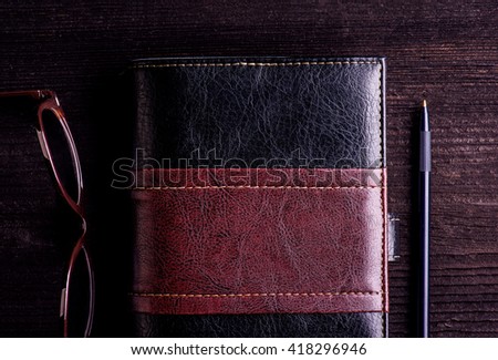 Book, eyeglasses and pen laid on old wooden table