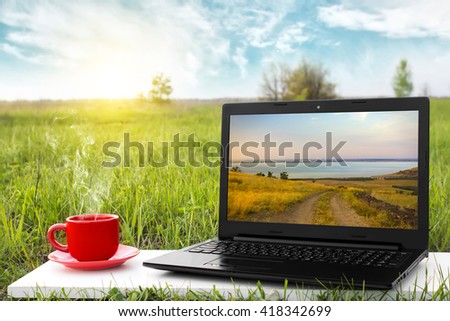 Laptop and cup of hot coffee on the background picturesque nature, outdoor office. Travel concept. Business ideas. The rest of nature. Beautiful landscape.