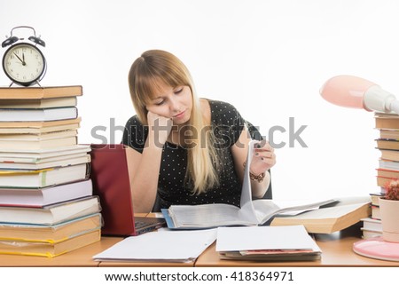 Student sadly looking at turning the pages in a folder at the desk among the stacks of books