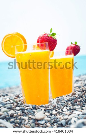 Orange fresh cocktail on the beach. Two glasses with juice decorated with strawberry. Holiday on the beach in summer. 