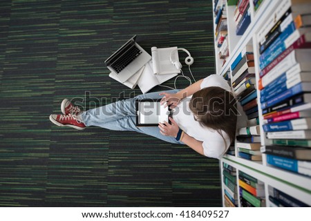 female student study in library using tablet and searching internet while  Listening music and lessons on white headphones Royalty-Free Stock Photo #418409527