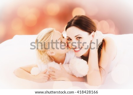 Cute little girl kissing her mother against glowing background